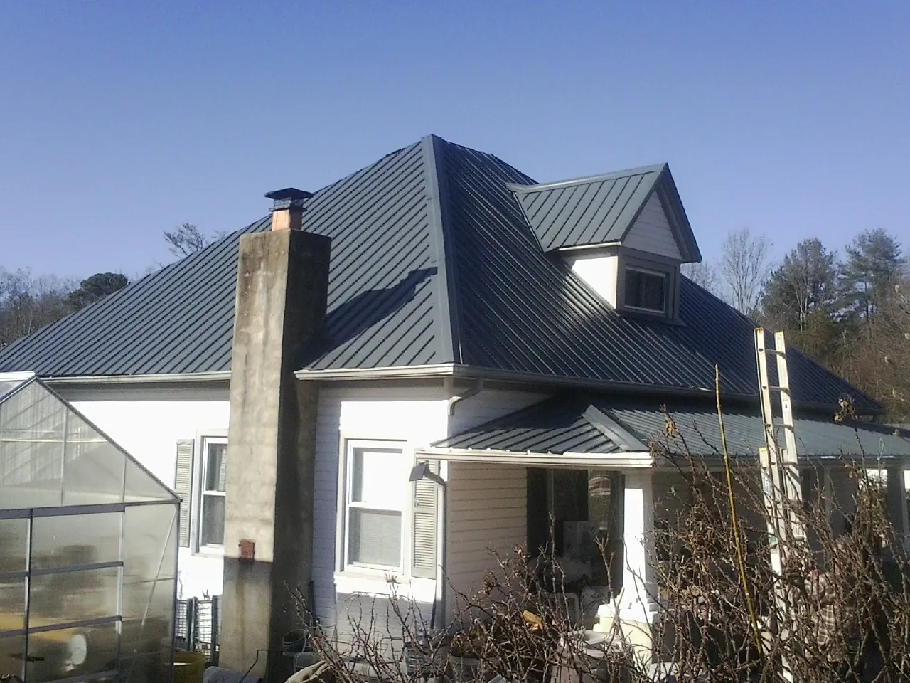 Dark blue standing seam metal roof on a white farmhouse with dormer — Slate & Tile Roof Repair by Roofing Brothers in West Eaton