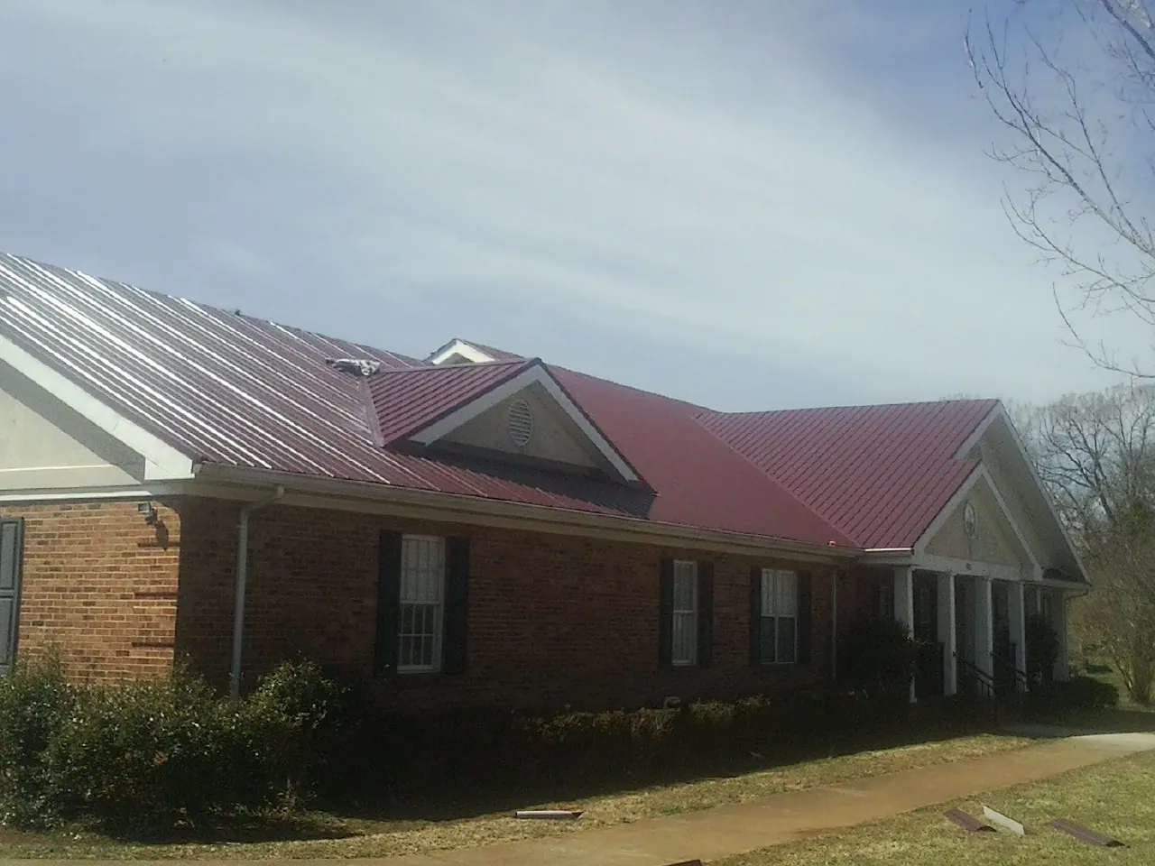 Red metal roof with gabled entries on a long brick building, from a Hail Damage Roof Repair job in West Eaton