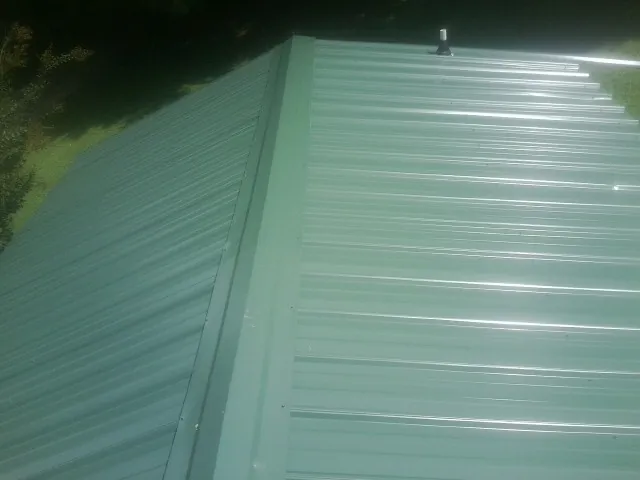 New green metal panels meeting at the ridge of a roof — Flat Roof Repair work by our crew in West Eaton