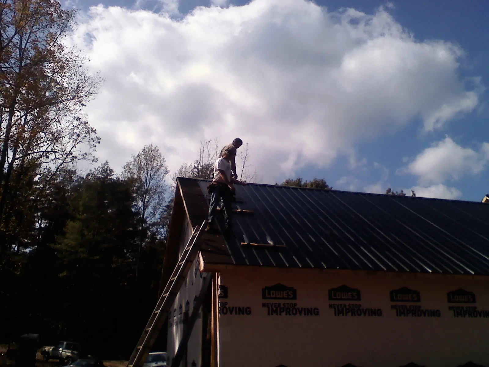 Roofer fastening dark metal panels high against a cloudy sky, from a Roof Inspection job in West Eaton