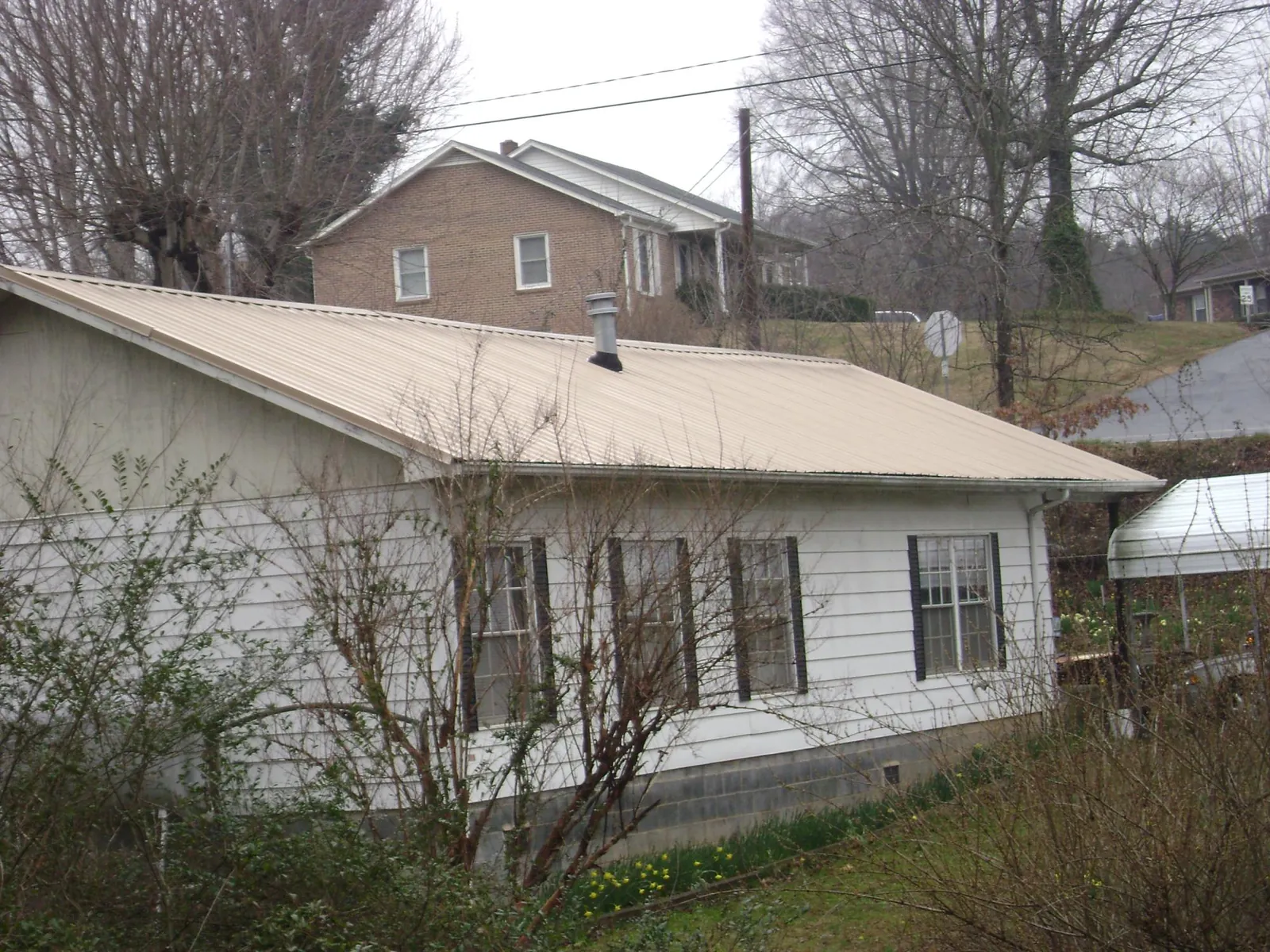 Tan metal roof on a white sided house set into a hillside — Commercial Roofing by Roofing Brothers in West Eaton